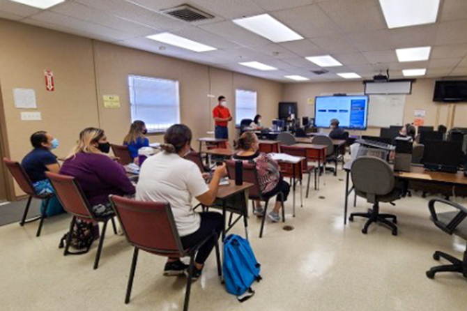 Students sitting in a classroom socially distanced listening to a speaker at the front of the class