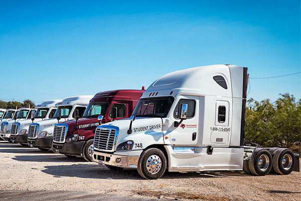 Row of Southwest Texas College student driver semi-trucks parked outdoors at the college's commercial truck driving training facility.