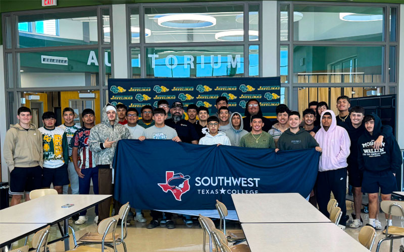 Vice President of Student Services Cruz Mata stands alongside the Crystal City High School Javelina football team holding a Southwest Texas College banner.
